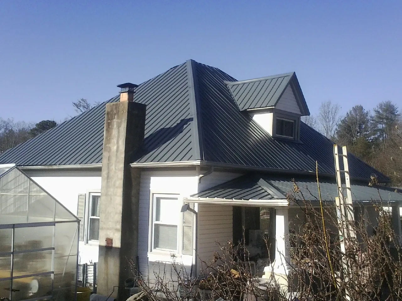 Dark blue standing seam metal roof on a white farmhouse with dormer — Slate & Tile Roof Repair by Roofing Brothers in Bagley
