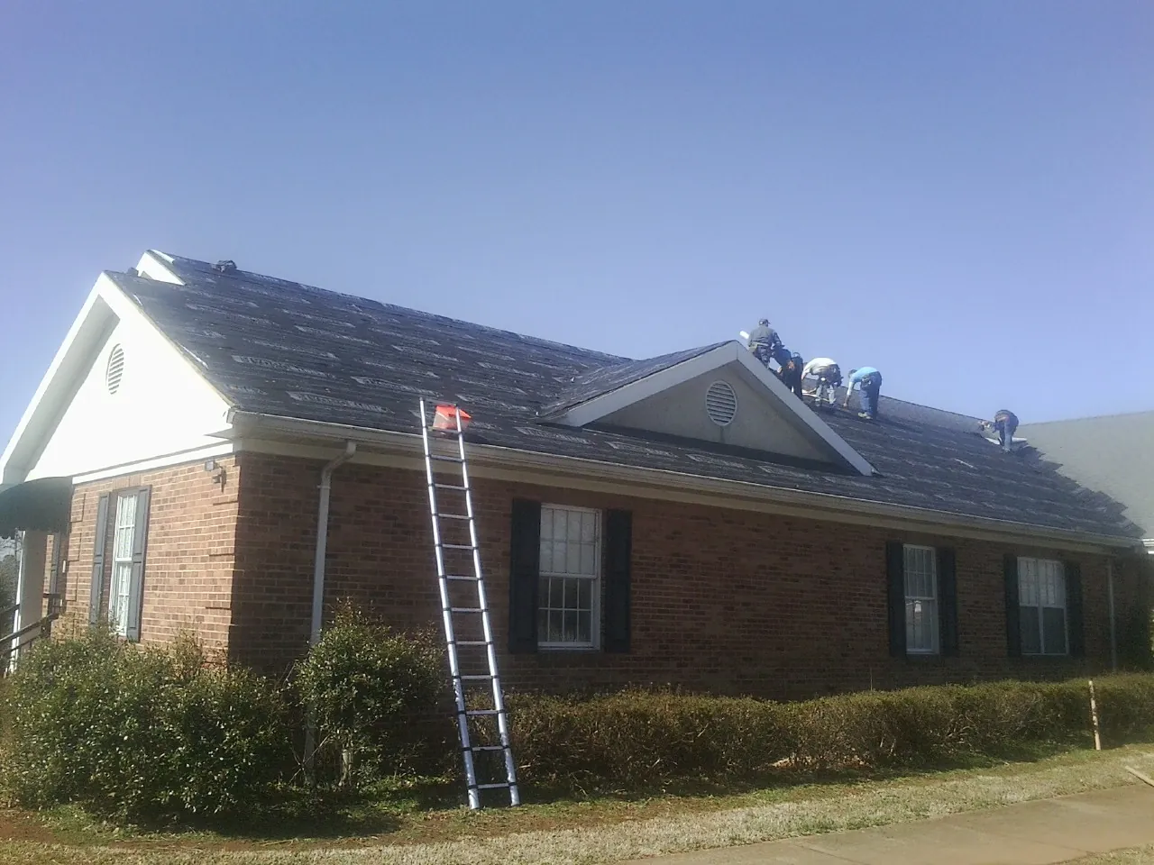 Crew tearing shingles off a brick ranch roof with a ladder set — Metal Roof Repair work by our crew in Bagley