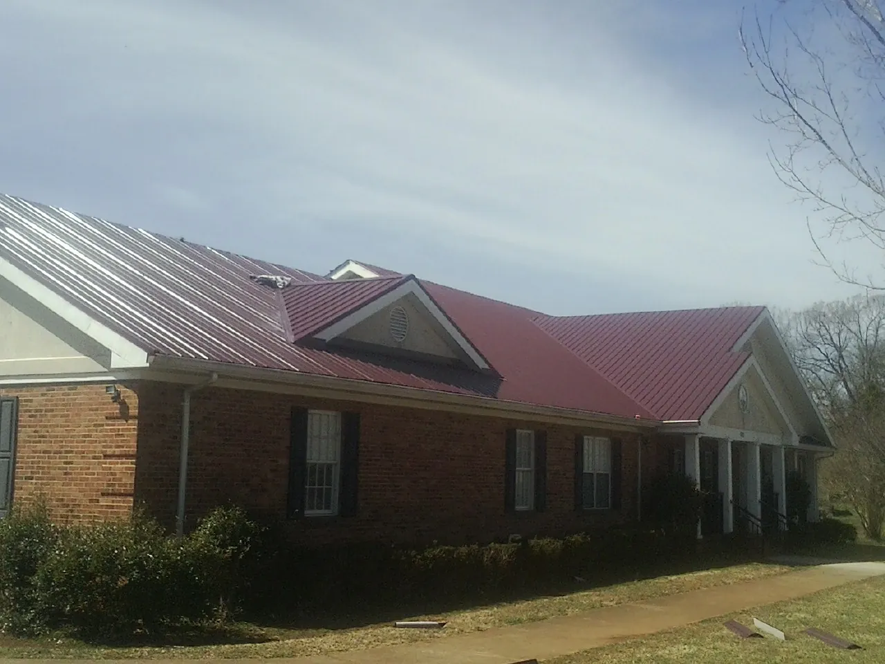 Red metal roof with gabled entries on a long brick building, from a Hail Damage Roof Repair job in Bagley