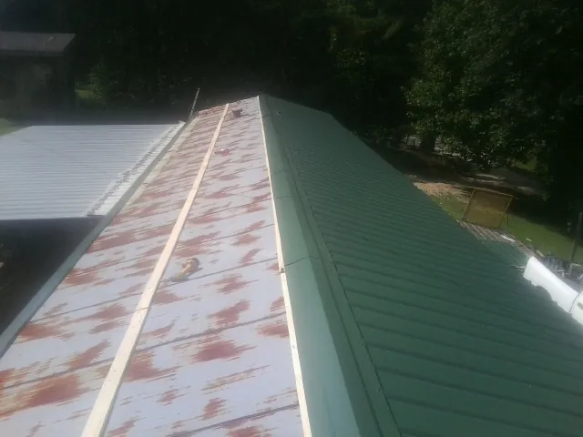 Old rusted panels beside newly installed green metal roofing — Wind Damage Roof Repair by Roofing Brothers in Bagley
