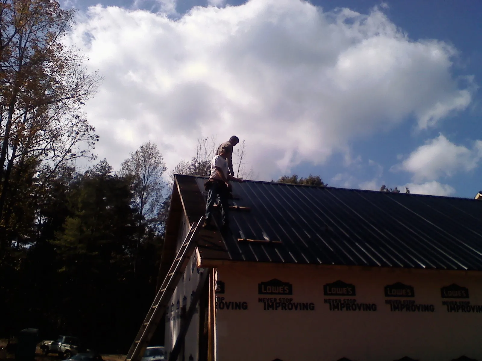 Roofer fastening dark metal panels high against a cloudy sky, from a Roof Inspection job in Bagley