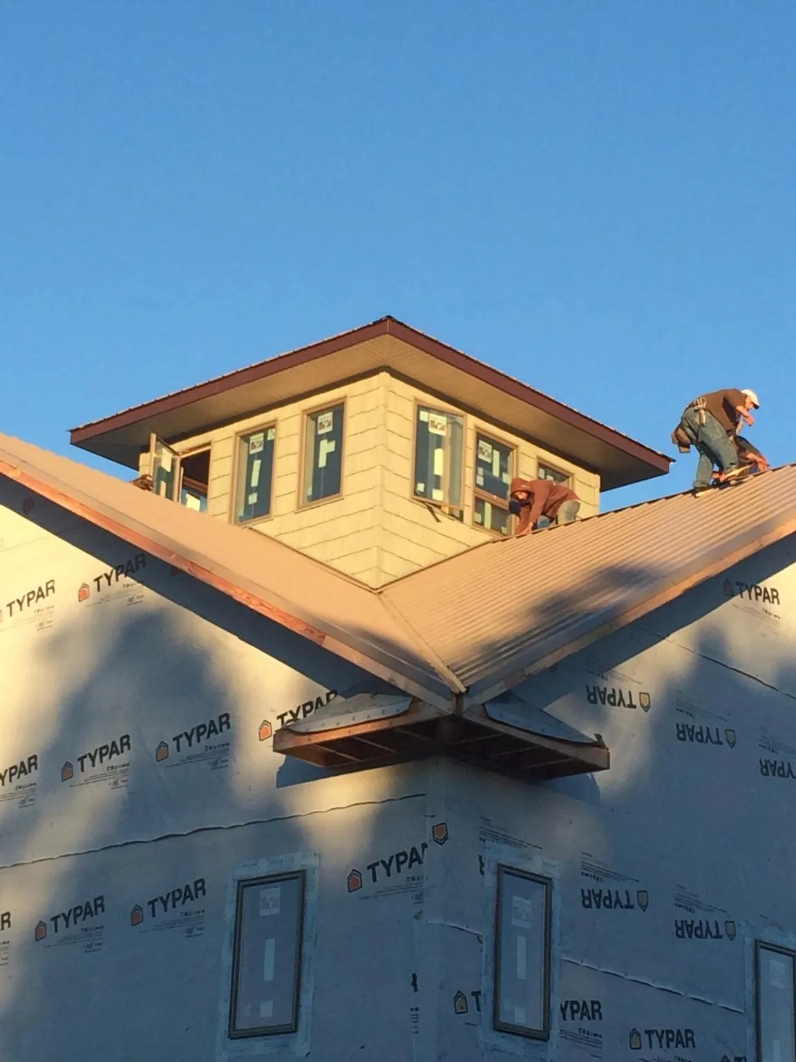Roofers working around a rooftop cupola on a new metal roof at sunset — Roof Waterproofing in Bagley by Roofing Brothers